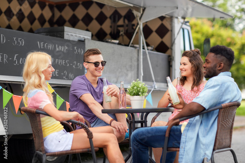 leisure and people concept - happy friends with drinks sitting at table at food truck