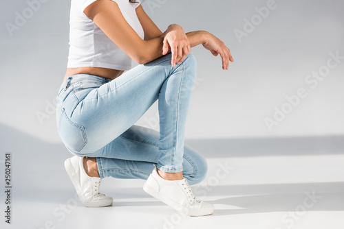 Cropped view of stylish woman in jeans sitting on grey background photo