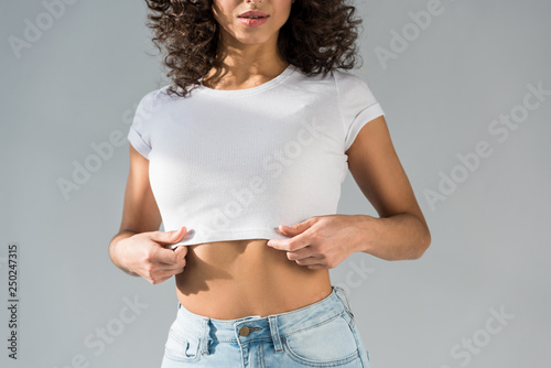 Cropped view of sexy curly woman in crop top isolated on grey