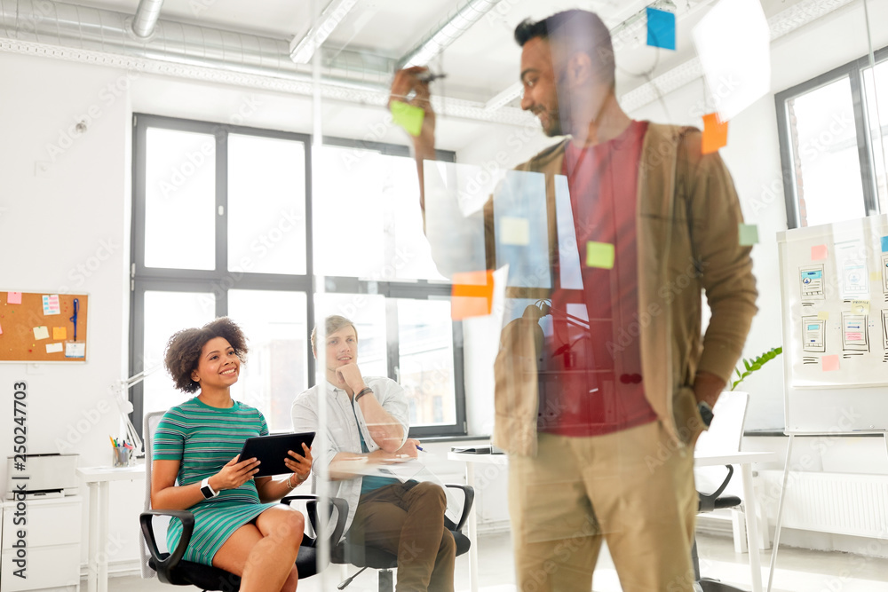 business, startup, planning and people concept - man at glass board showing something to creative team at office presentation