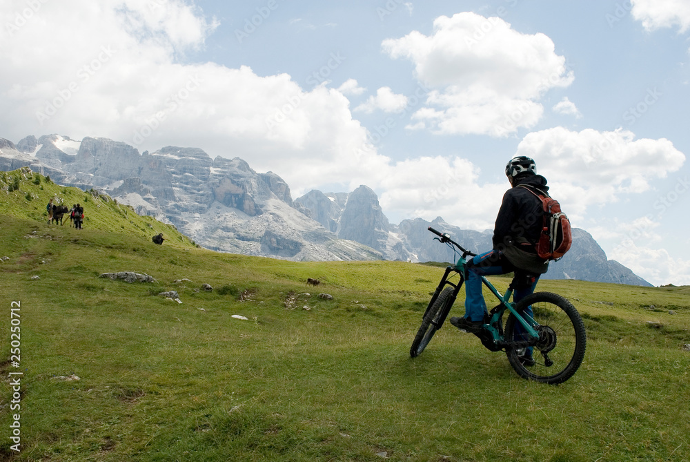 man with an electric bike, e-bike, ebike, mountains of Cima Tosa and Brenta Peak, meadow, Dolomites, unesco heritage, Madonna di Campiglio, sport, adventure, travel, Alps, Trentino, Alto Adige, Italy