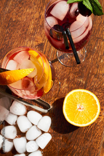  two cocktails aperol and kir royal on a wooden table, a half an orange and a bucket with ice are next to it. direct sunlight
