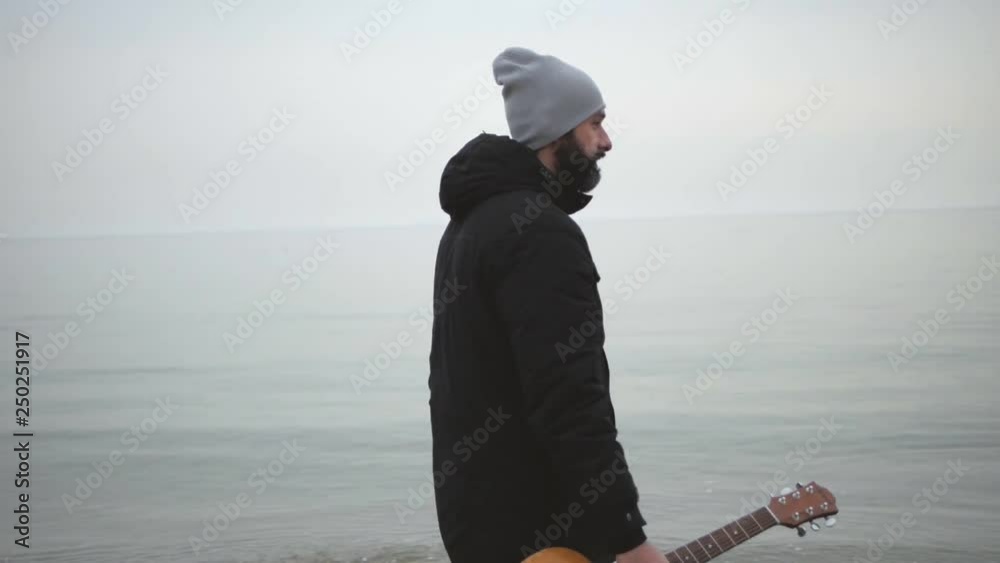 bearded man with a guitar walking along the beach bearded man with a guitar walking along the beach