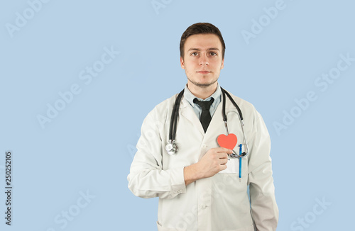 european doctor in a dressing gown with a red heart in his hands on an isolated blue background.The concept of health, gifts and holidays