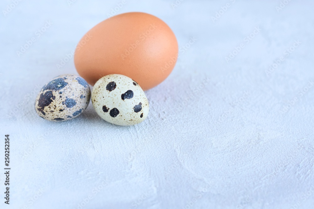 Brown Easter egg and spotted quail egg with selected focus on structured cement background. Happy easter holiday card with empty space for text. Pattern eggs on gray textured backdrop 