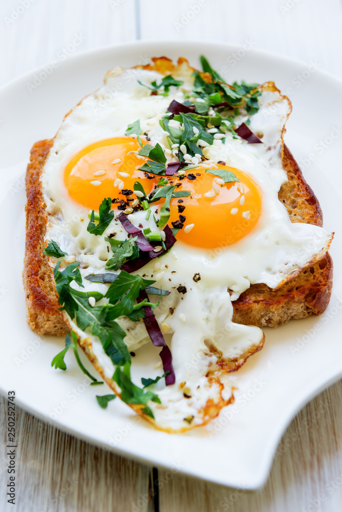 Fried egg with two yolks on bread with chopped greens on a white dish view from the top