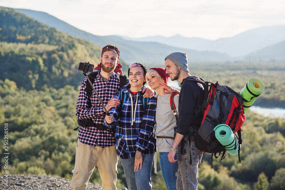 Group of young smiling people traveling together in mountains. Happy hipster travelers with backpacks making selfie. Traveling, tourism and friendship concept.