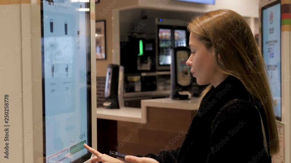 Woman customer store place orders and pay by contactless credit card mobile phone through self pay floor fast food, payment terminal touchscreen big cafe. Paypass.