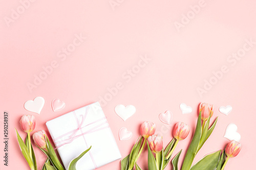 Romantic floral background with tulips flowers, gift and hearts on pink pastel background.