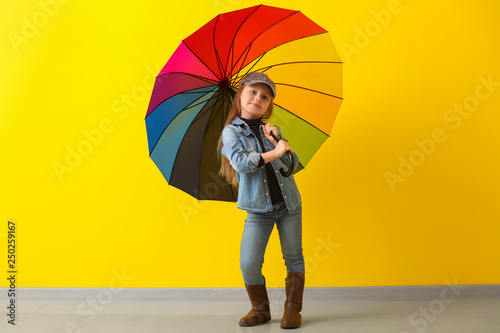 Stylish little girl with umbrella near color wall