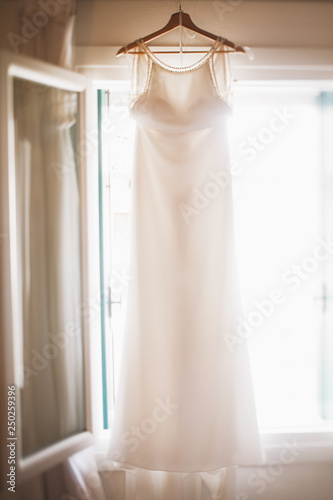 Beautiful wedding dress hangs before the bright window