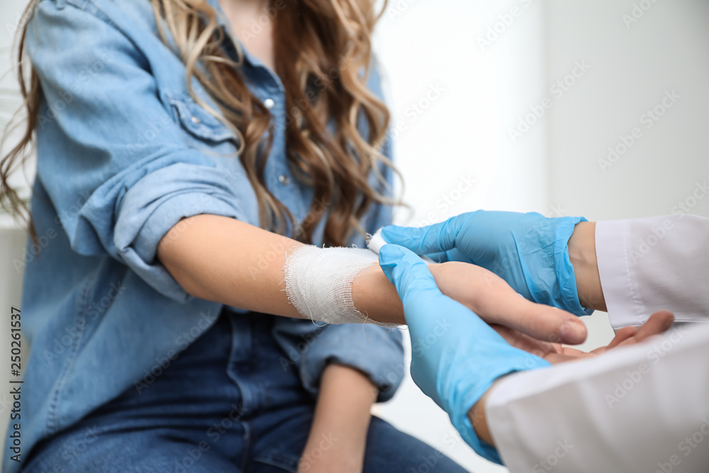Doctor applying bandage onto wrist of young woman