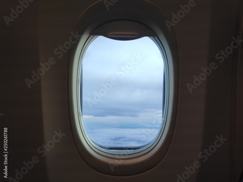 Airplane window with sky clouds view.