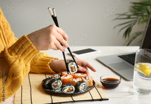 Woman eating tasty sushi rolls at home