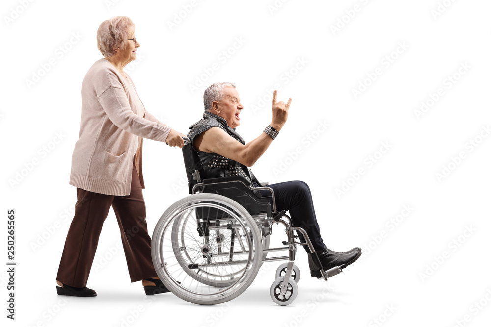 Elderly woman pushing a mature man making a rock and roll hand sign in a wheelchair Elderly woman pushing a mature man making a rock and roll hand sign in a wheelchair