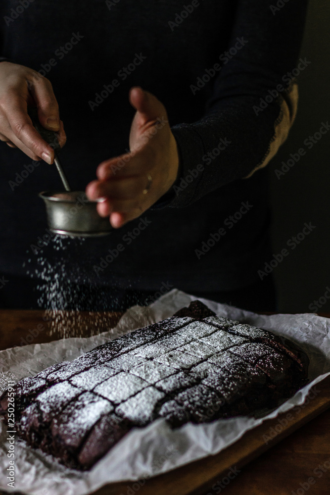 Obraz premium Woman sprinkling powdered sugar on top of brownie