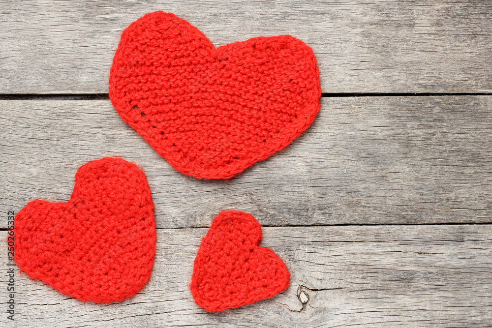 Obraz premium Three red knitted hearts on a gray wooden background, symbolizing love and family