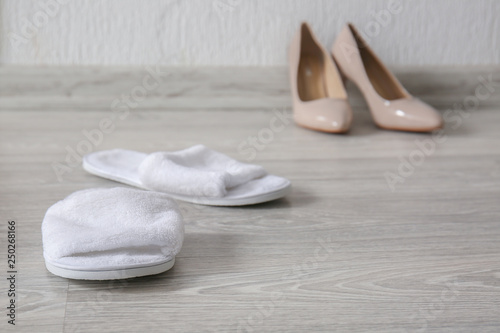 Comfortable slippers and high heeled shoes on floor