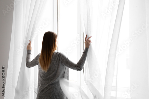 Young woman opening curtains in morning