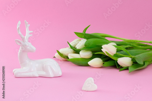 White tulips with deer and heart shaped stone on pink background. Flower flat lay  side view. Floral concept