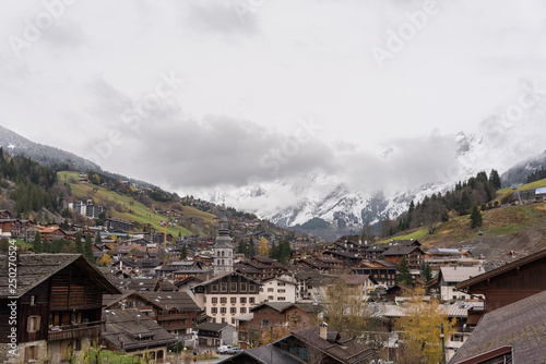 Alpine village with high bell tower on the background of the Alps