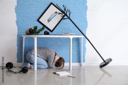 Young woman hiding under table during earthquake photo