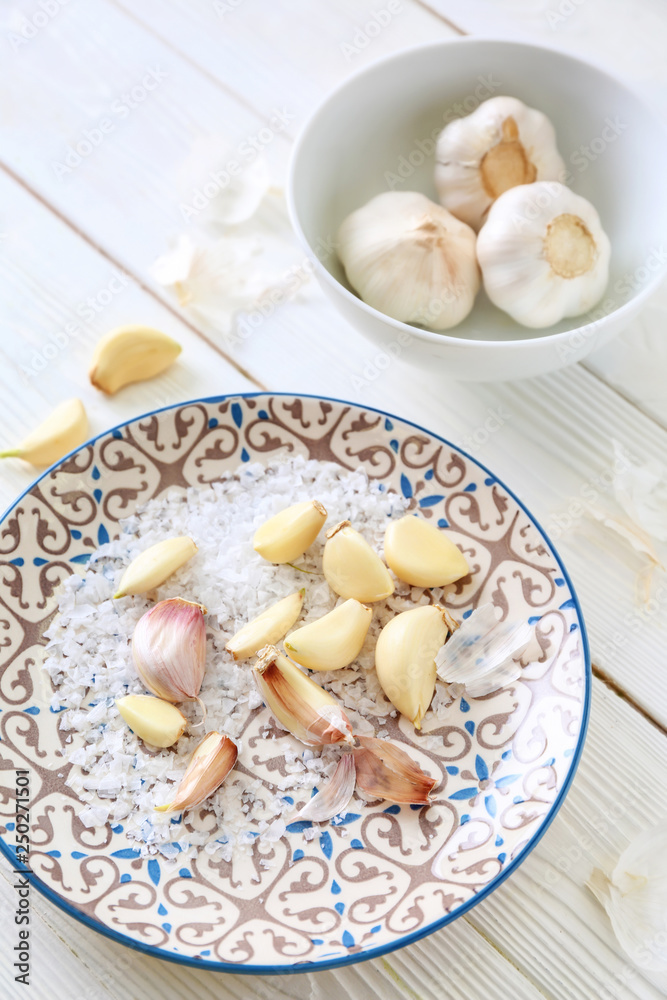 Plate with fresh garlic and salt on white wooden background Plate with fresh garlic and salt on white wooden background
