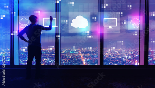 Cloud computing with man writing on large windows high above a sprawling city at night