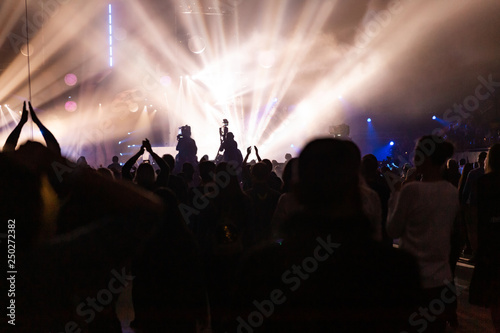 Silhouettes of a concert crowd and cameraman against the background of bright, colorful rays on the stage. © Roman Rvachov