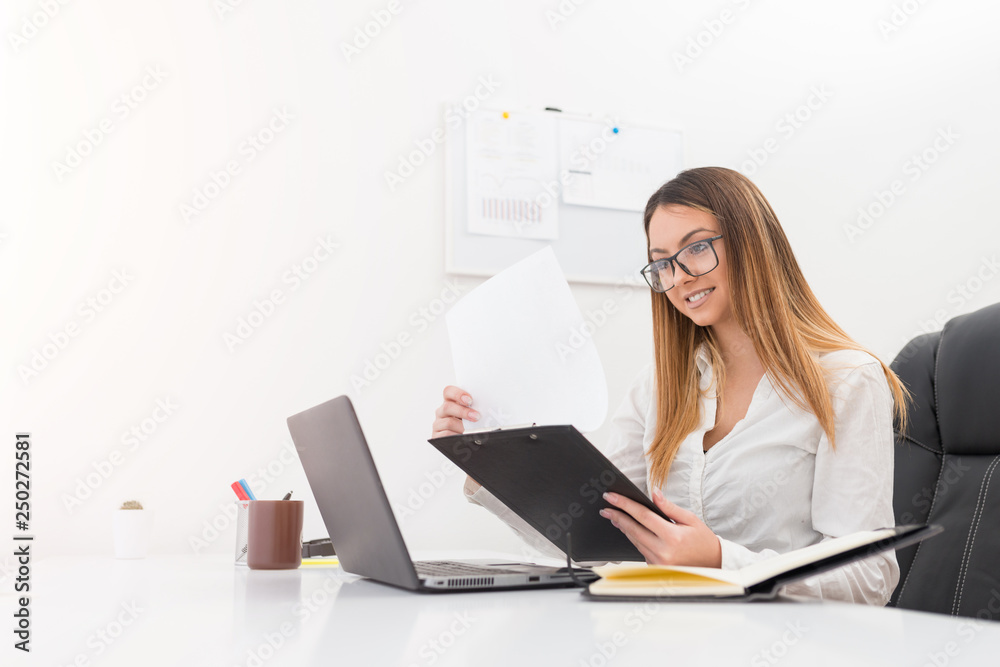 Pretty cheerful young manager woman looking in charts in her office. Pretty cheerful young manager woman looking in charts in her office.