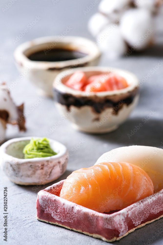 Sushi Set nigiri with salmon and butterfish in pink ceramic serving plate with bowls of soy sauce and pickled ginger, cotton flowers on light blue table. Japan menu Sushi Set nigiri with salmon and butterfish in pink ceramic serving plate with bowls of soy sauce and pickled ginger, cotton flowers on light blue table. Japan menu