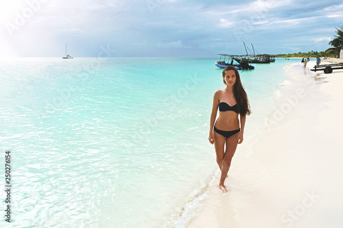 Attractive slim brown-haired woman in a bikini on a white sandy paradise beach Kendwa of Indian Ocean of Zanzibar island
