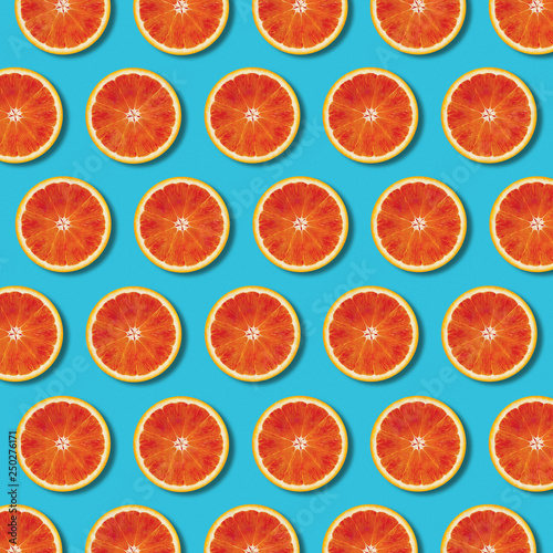 Red orange slices pattern on vibrant turquoise color background. Minimal flat lay top view food texture 