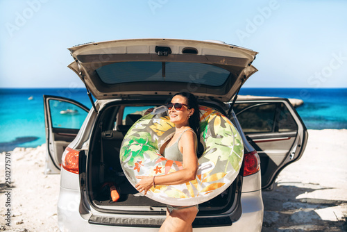 Pretty pan asian brunette with float near car trunk at the seaside beach.