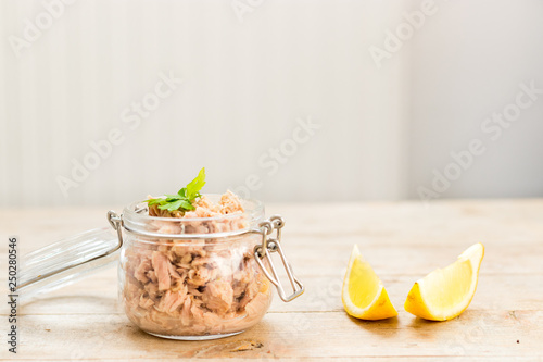 Fresh raw tuna in a glass mason jar with lemon slaces on a wooden table. Minimal style home made healthy food concept. photo