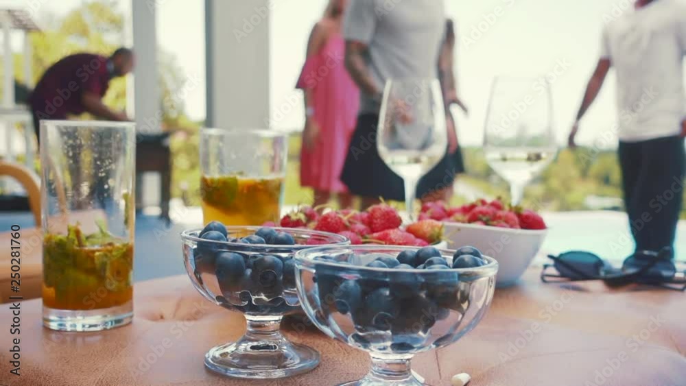 Blurred background with dancing and fun people on pool villa with view and alcohol drinks cocktails with berries on foreground Blurred background with dancing and fun people on pool villa with view and alcohol drinks cocktails with berries on foreground
