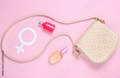 Leather bag, gender symbol of women, perfume bottles on pastel pink background. Top view