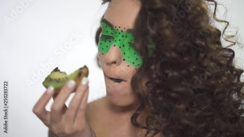 Close up portrait of young beautiful curly girl with creative make up eating kiwi. photo