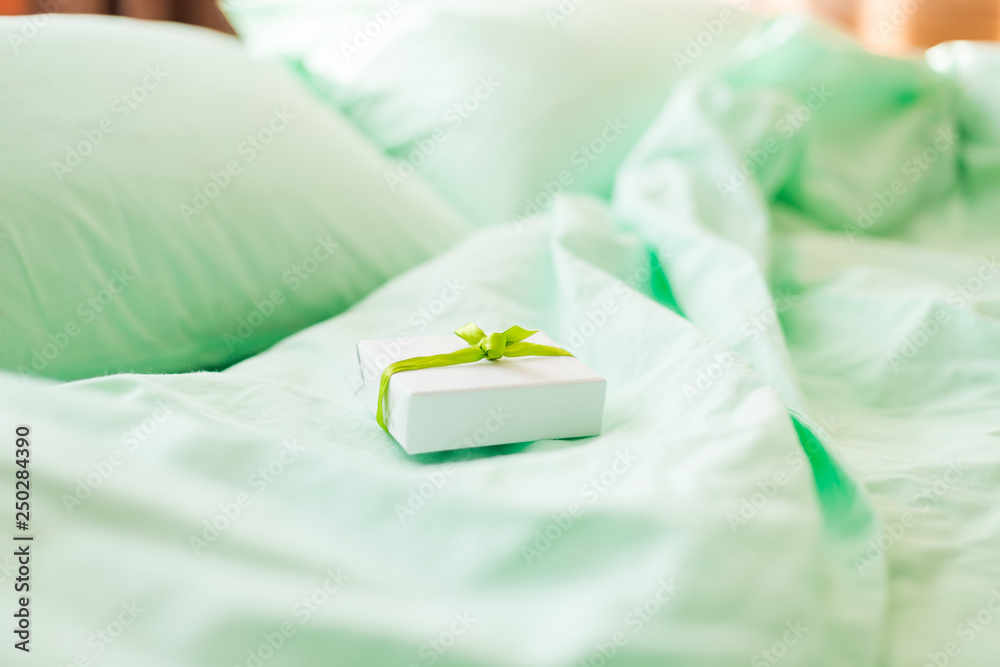 A small white gift box on minty green bed in the morning. A small white gift box on minty green bed in the morning.