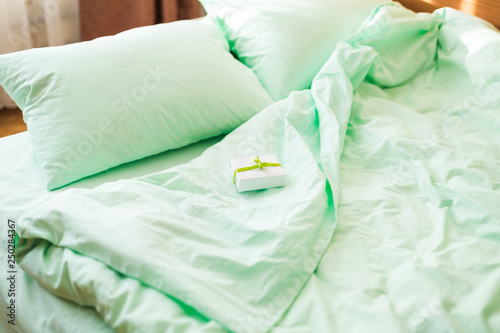 A small white gift box on minty green bed in the morning.