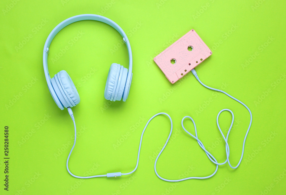 Blue headphones with cable in audio cassette on green background. Minimalism. Top view Blue headphones with cable in audio cassette on green background. Minimalism. Top view