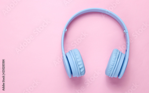 Modern wireless blue headphones on a pink pastel background. Top view. Copy space
