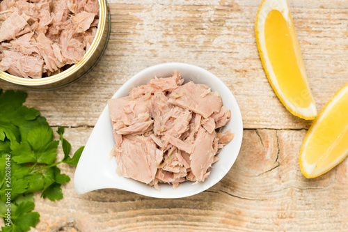 Premium quality canned tuna in a white bowl with lemon and another opened tuna can. Close up of a high quality preserved sea food.