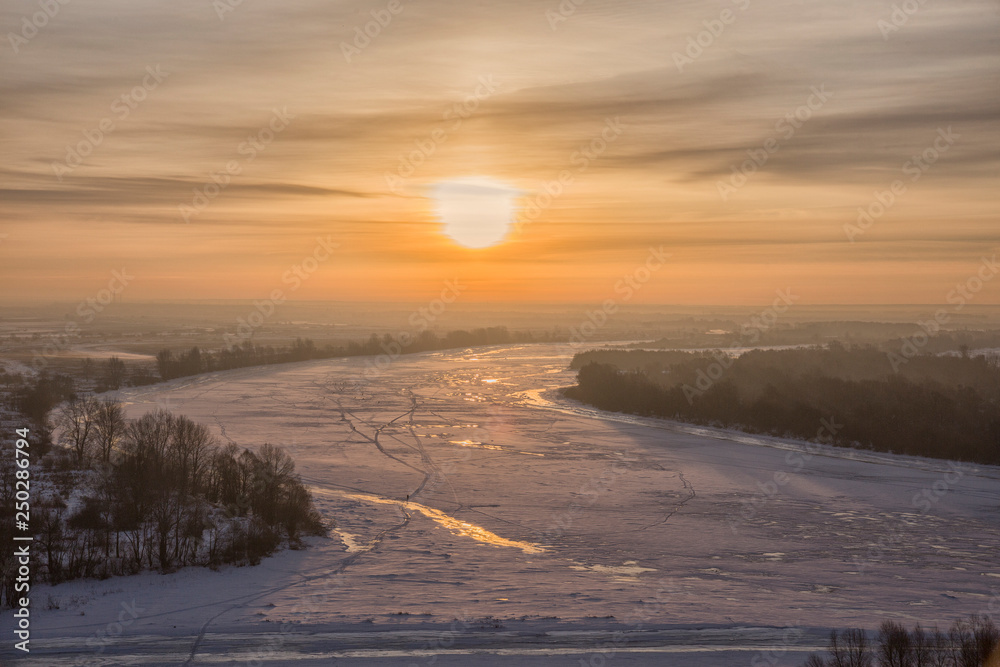 Panoramic view on frozen river and forest on hill in winter during sunset from hill
