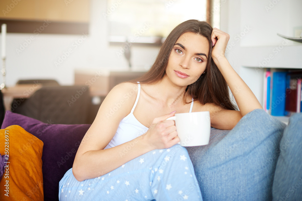 Beautiful young woman holding mug in her hand while relaxing on sofa at home Beautiful young woman holding mug in her hand while relaxing on sofa at home