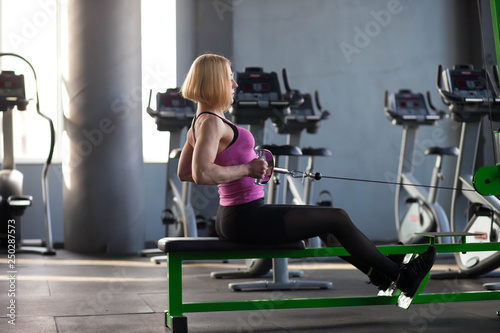 Athletic mature woman doing exercises with rowing machine at gym. Healthy lifestyle concept