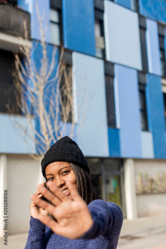 Fototapeta premium Young beautiful black woman standing outdoors in the city using a phone while looking camera and forbids
