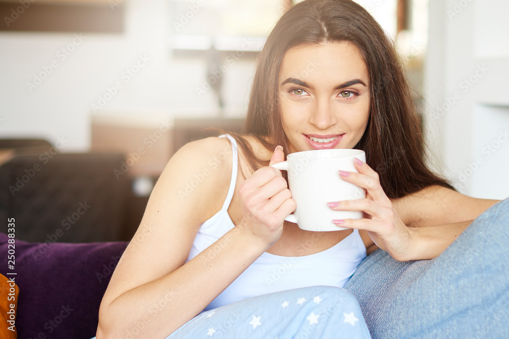 Beautiful young woman holding mug in her hand and daydreaming at home Beautiful young woman holding mug in her hand and daydreaming at home