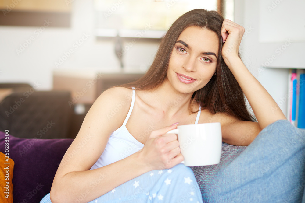 Beautiful young woman holding mug in her hand while relaxing on sofa at home Beautiful young woman holding mug in her hand while relaxing on sofa at home