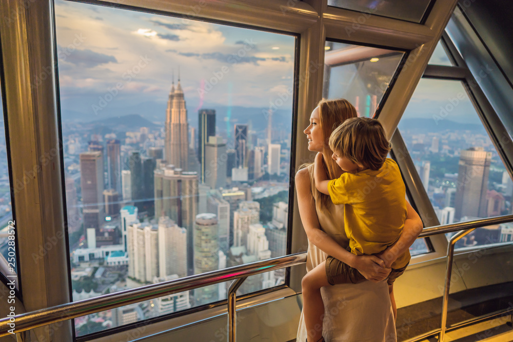 Fototapeta premium Mom and son are looking at Kuala lumpur cityscape. Panoramic view of Kuala Lumpur city skyline evening at sunset skyscrapers building in Malaysia. Traveling with kids concept